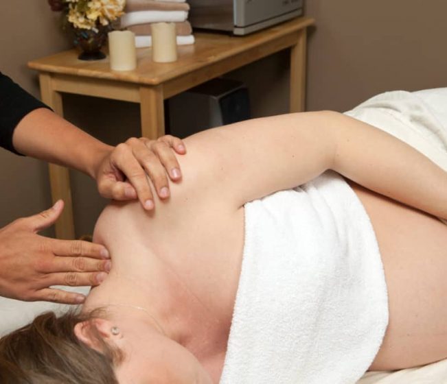 A pregnant woman is receiving a prenatal massage from a female massage therapist. This type of massage is used to relieve tension, stress and discomfort during pregnancy.